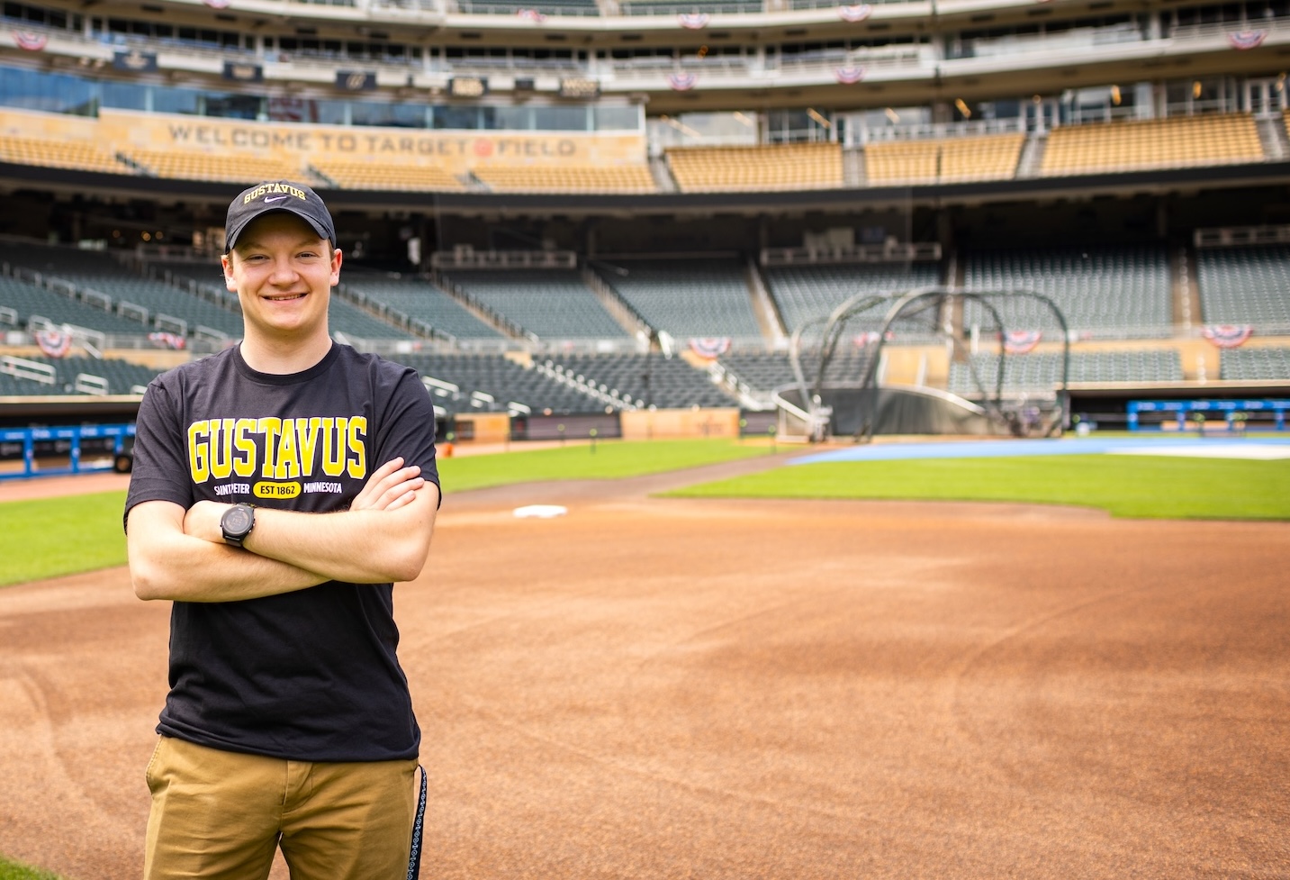 A student in a Gustavus t-shirt stands in the outfield of a baseball stadium.